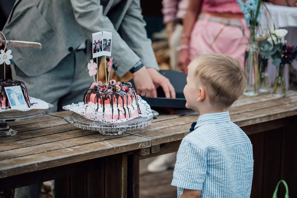 Kleiner Junge schaut auf eine Hochzeitstorte mit Beeren auf der Holzbar