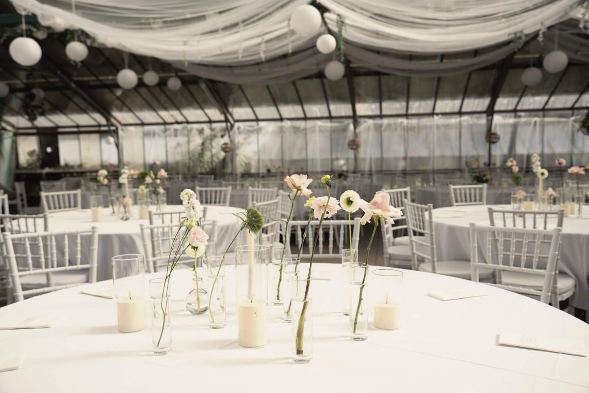 Runder Tisch mit einzelnen Blumen in Glasvasen und Kerzen im Gewächshaus